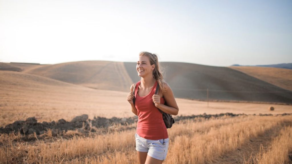 Smiling woman in casual attire enjoying a summer hike through golden fields at sunset.