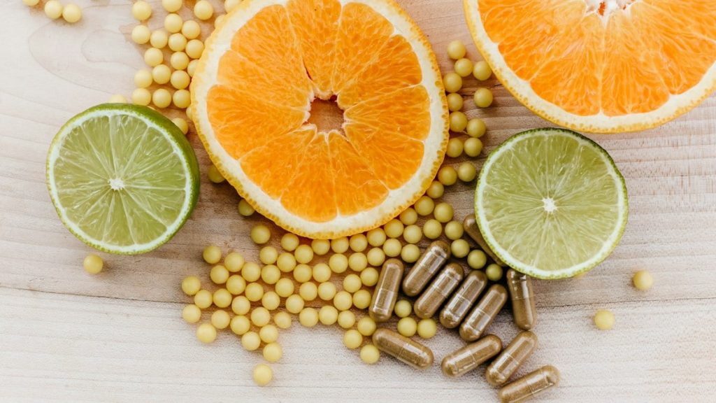 Citrus slices, small yellow supplement beads, and brown capsules on a wooden surface